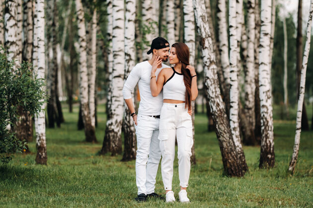 时尚一对穿着白色衣服的年轻漂亮的夫妇在桦树林的背景下健康早晨夜晚