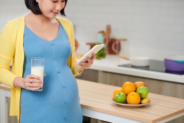饮食拿着一杯牛奶的年轻孕妇站在厨房里乳制品营养厨房
