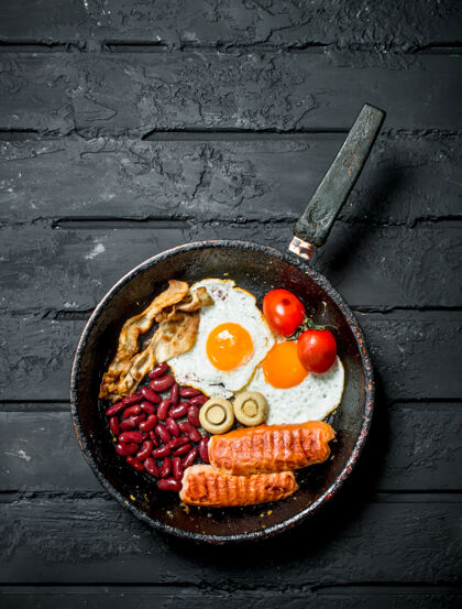 一餐传统的英式早餐在黑色乡村餐桌上的平底锅里培根切片不健康