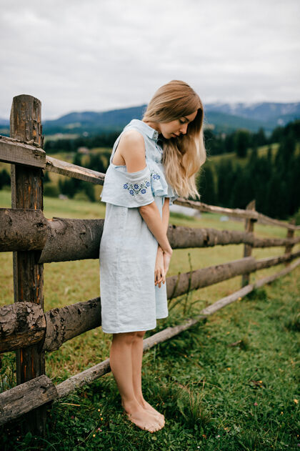 夏天年轻漂亮的金发碧眼的女孩 穿着蓝色的裙子 在乡村的篱笆边摆姿势如画女孩女人
