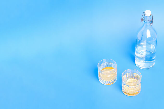 微量玻璃与水和柠檬接近瓶子上的蓝色背景与复制空间瓶装柠檬水液体