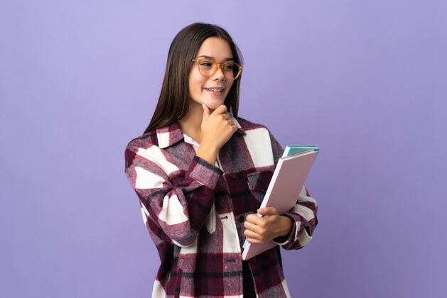 大学年轻的女学生孤零零地站在紫色的一边微笑着看着身边眼睛教育笔记本