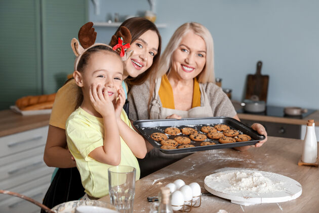 庆祝年轻女子带着她的小女儿和妈妈在家做圣诞饼干房子孩子糕点