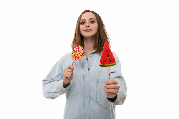 模型一个穿着牛仔衬衫的年轻女子摆出彩色棒棒糖的姿势时尚甜点甜