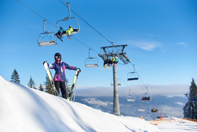 休闲快乐的女人站在雪山坡上的电梯旁 手里拿着滑雪板寒假的晴天总览电梯娱乐户外