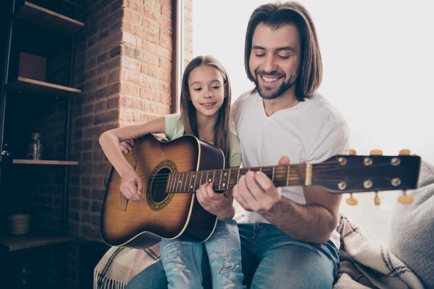 玩耍可爱的小女孩和帅气迷人的年轻爸爸的照片坐在窗台上拿着原声吉他学习新的部分歌曲花时间在室内音乐室休闲音乐吉他
