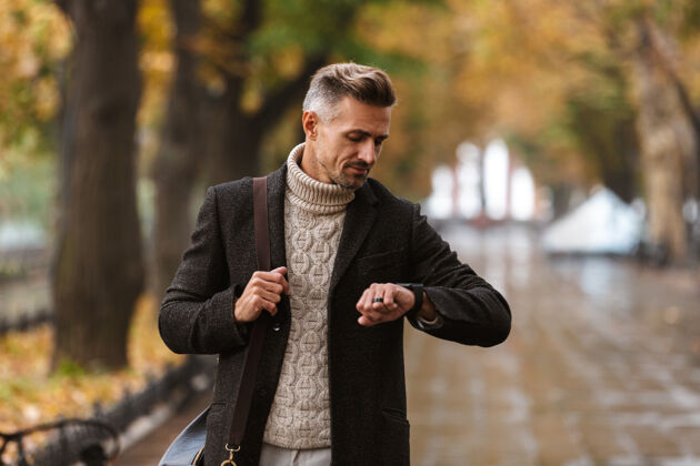 肌肉30多岁的帅哥穿着暖和的衣服在户外穿过秋园 看着手表的照片帅气胡须散步