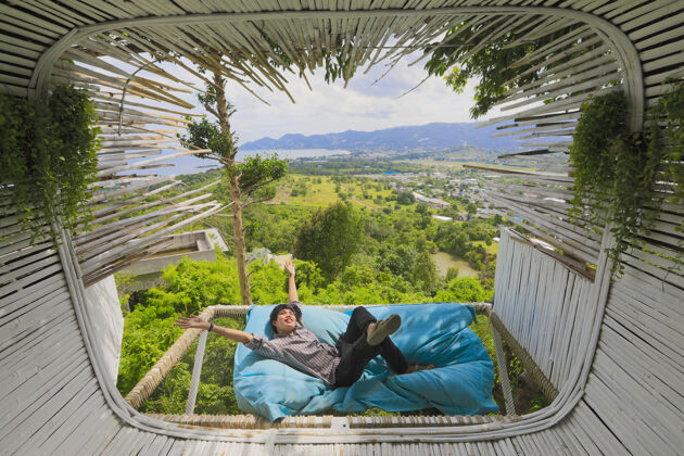男性亚洲男子躺在沙发床上亚洲游客躺在露天咖啡厅靠近露台的沙发床上 窗外风景优美山时间放松点自由山丘亚洲