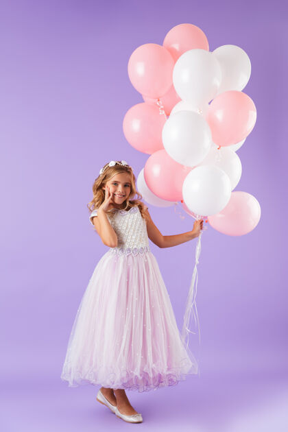 肖像一个穿着公主裙的漂亮小女孩孤零零地站在紫罗兰色的墙上 手里拿着一堆气球长度五颜六色白种人
