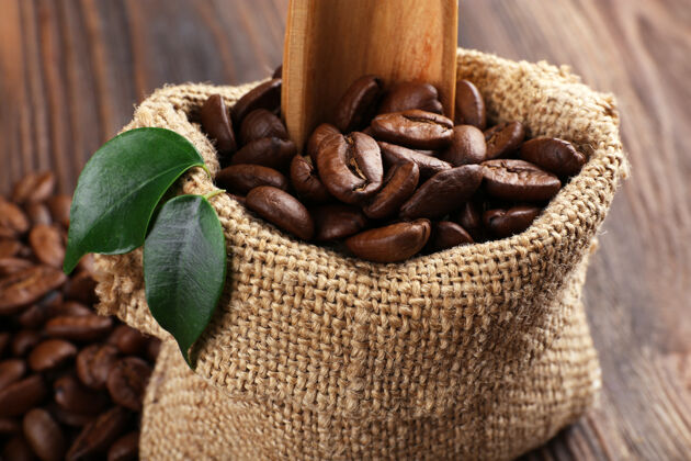 阿拉伯语咖啡豆叶子和勺子放在木桌上的袋子里特写早餐新鲜木材