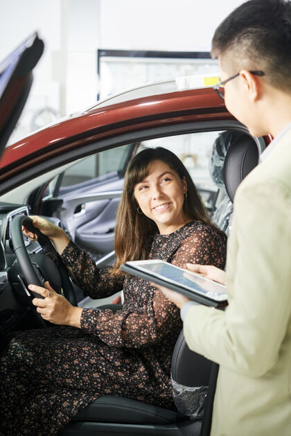 坐席微笑的女人坐在车里 在汽车沙龙里和推销员讨论保险的一些细节沙龙平板电脑女士