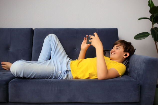 房子带着智能手机和耳机在家里用手机听音乐或玩游戏的青少年玩家注意孩子