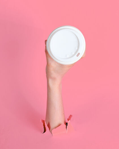 马克杯女性的手拿着纸咖啡杯穿过撕破的粉红色纸简约概念包装通过带走