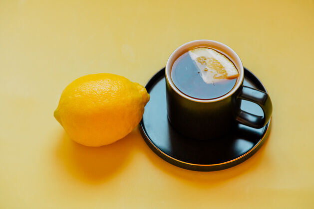 马克杯柠檬茶茶把一片柠檬放在茶碟上的黑杯子里柠檬食物健康