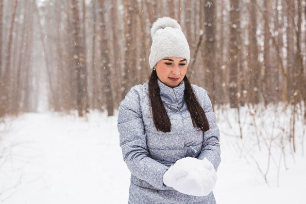 年快乐的年轻女子在冬季公园里拿着雪冬天女人微笑