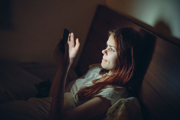 在线晚上 女人从床上爬起来 手里拿着一部电话休息虚拟房间女性通讯放松