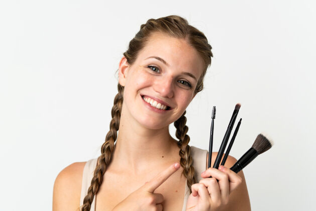 化妆一位年轻的白人女性 手拿化妆刷 指着它 孤立地站在白色的背景上快乐女性模特