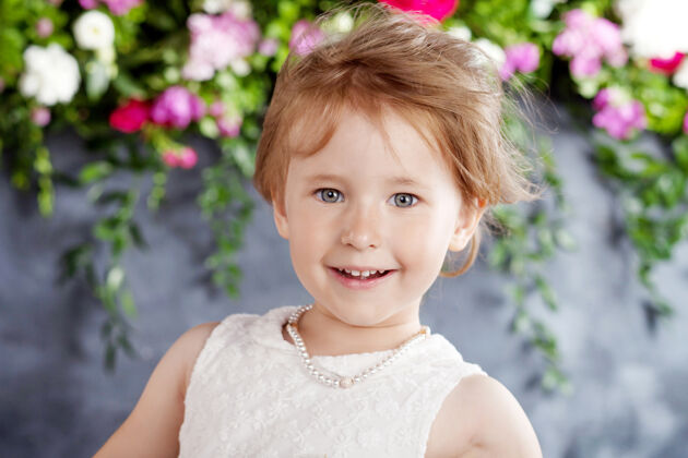 微笑可爱的小女孩的肖像花看对着镜头快乐美丽服饰
