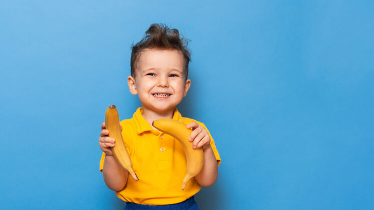 小快乐的肖像画 一个孩子带着迷人的微笑 穿着黄色t恤 手里拿着一根香蕉 在摄影棚拍摄微笑有机水果