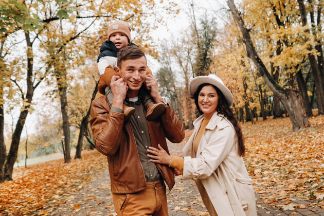 散步爸爸和妈妈带着儿子在秋天的公园里散步一家人在金秋的自然公园里散步儿子树叶三