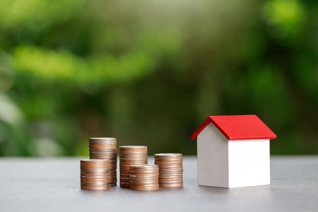 销售房地产投资和房屋抵押贷款的金融概念 硬币堆与绿色背景下的房屋模型付款家庭预算