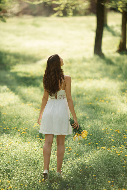 女士后视图：一位身着白色连衣裙的迷人女士 迎面走来一束春花化妆花束花园