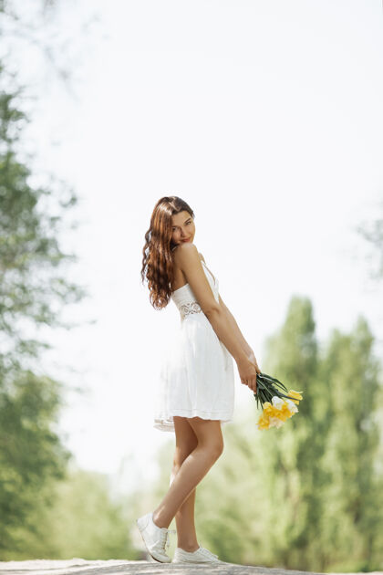 吸引力一位身着白色连衣裙 手持一束春花的迷人女子 站在大自然的衬托下微笑树亚洲