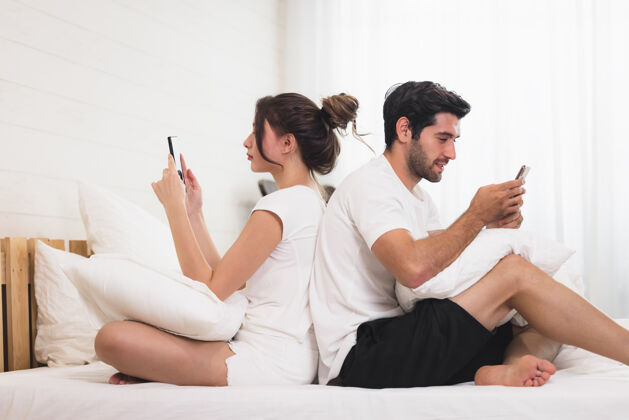 家庭千禧一代夫妻在吵架 背靠背地躺在床上 用手机男性看信息