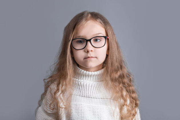 可爱一个年轻漂亮的小女孩的肖像 金发飘逸 穿着白色毛衣 在灰色的工作室里微笑背景.地点为了文本.复制空间人类孩子生活方式