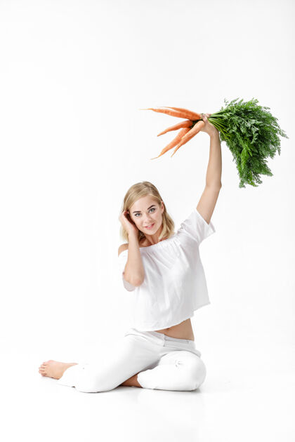 美丽一个穿着白衬衫的金发美女 手里拿着一根新鲜的胡萝卜 上面有绿叶背景.健康还有节食素食胡萝卜快乐
