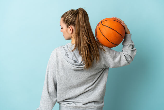 篮球年轻的白人女子孤立在蓝色背景下打篮球在后面的位置位置比赛运动