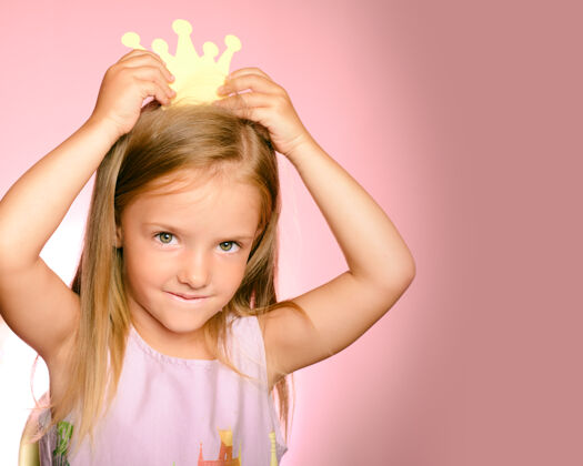 站美丽的金色皇后小皇冠戴着黄色皇冠的公主女孩 粉色背景上的漂亮裙子房间服装欢乐
