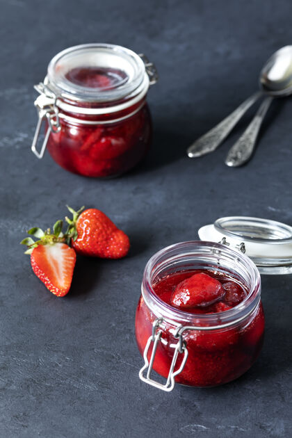勺子一罐罐自制草莓酱 配上成熟的草莓和勺子放在黑暗的表面上罐子草莓甜点