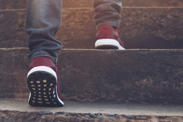 跑步楼梯关闭上身牛仔裤和鞋子运动鞋红色的年轻时髦男人一个人走上楼梯在现代城市 上楼梯 成功 成长向上阳光在早上时髦散步目标