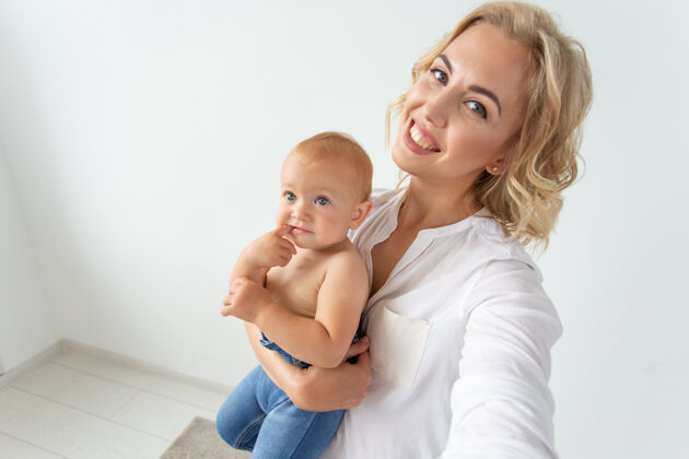 可爱家庭和母亲的概念-快乐年轻的金发妈妈与小宝宝自拍拍照房子单身
