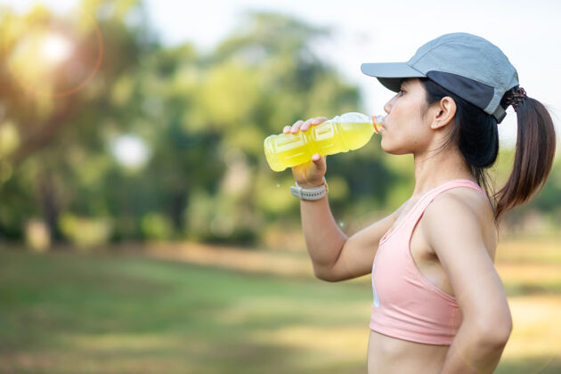 减肥年轻的健身女士在公园户外伸展肌肉时饮用能量水 亚洲运动员在公园跑步锻炼早上好运动健康理念健康新鲜快乐