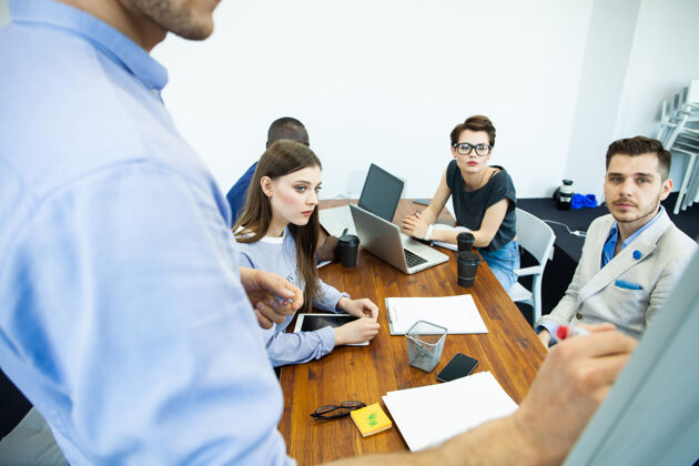 随意讨论公司进步自信年轻人站在白板旁边 指着图表 而他的同事坐在办公桌旁图表创意领导