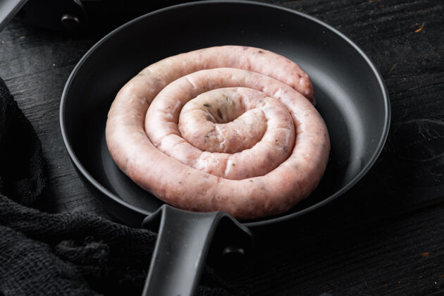 生的传统的生螺旋猪肉香肠放在铸铁煎锅里 放在黑木桌上猪肉美味德国