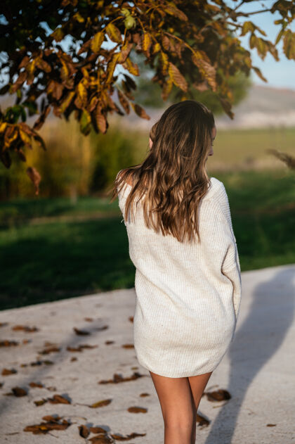毛衣秋日院子里 一位穿着白毛衣的匿名女性站在枯叶的树枝旁微笑柔软肖像