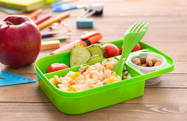 满满的木质背景的美味学校午餐盒蔬菜苹果文具