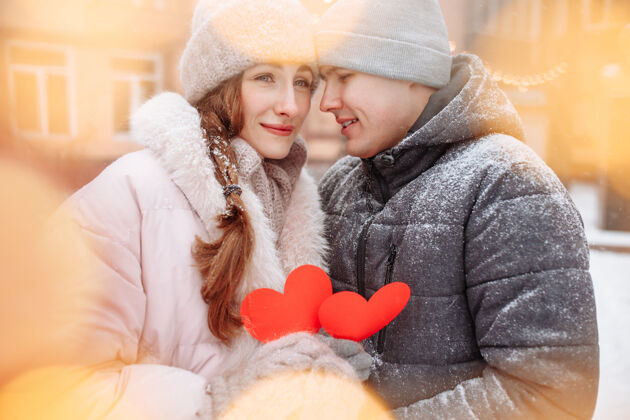 男人冬日里 一对年轻的情侣捧着红色的纸心 在外面感受着快乐和幸福爱情浪漫男人和女人在公园的雪下庆祝情人节享受手套惊喜