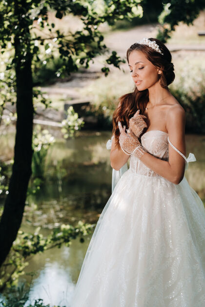 新娘一个优雅的新娘穿着白色礼服 戴着手套和花束在公园的瀑布上浪漫自由户外