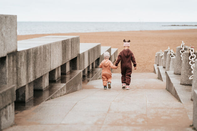 海洋两姐妹手牵手走到街上大海姐姐照顾孩子年幼儿童在海边散步凉爽白天友谊