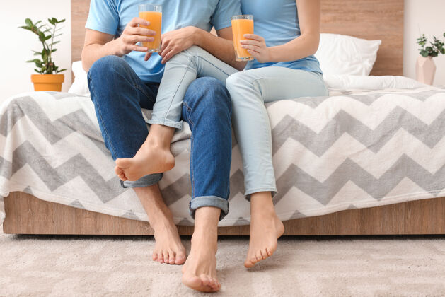女人一对喝着果汁的年轻夫妇坐在家里的床上早餐床赤脚