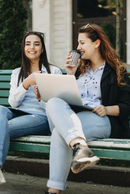 朋友美丽的年轻女孩坐在城外的长凳上 和她身材魁梧的女友讲故事视图移动互联网