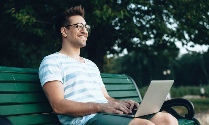 使用戴眼镜的白种人自由职业者在公园的长凳上对着电脑工作企业职业学习