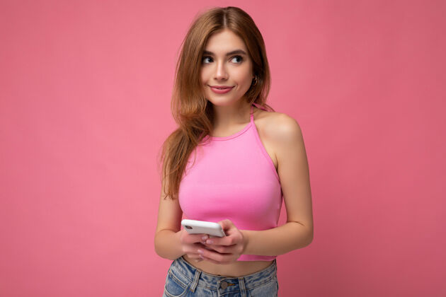浏览性感漂亮的金发女郎 穿着粉色上衣 站在粉色的墙上 空荡荡的空间里 手牵着手 用手机短信向旁边看思考互联网在线