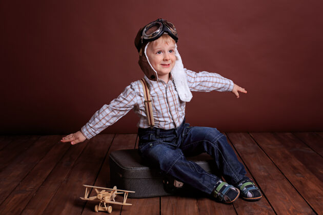 航空一个戴着飞行员头盔的小男孩和一个木头玩具玩飞机男孩穿着格子衬衫和吊带自由游戏房间