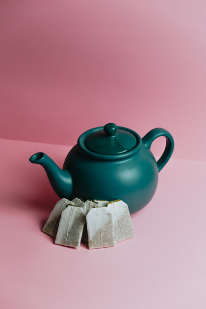 稀疏一个简约的蓝色茶壶和快速茶包在粉彩粉红色的背景上茶杯营销复古