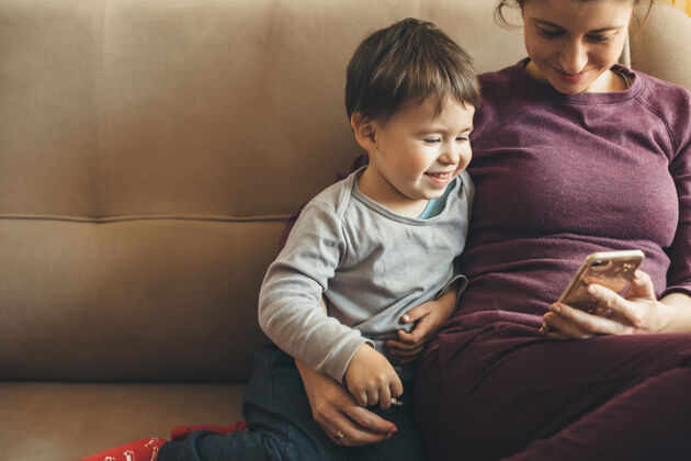 手机满脸雀斑的白人母亲和她的小男孩坐在沙发上 用手机人父母期望